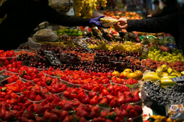Venta de deliciosas frutas a un comprador en el Mercado Central de Valencia (España), famosa por su huerta. Enfoque selectivo. Se ven las manos del comprador y del vendedor y la frescura de la fruta.