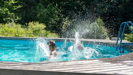 Two Caucasian girls aged 5-7 have fun swimming and splashing in the outdoor pool. Summer vacation in the backyard of the cottage.