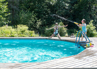 Two Caucasian girls aged 5-7 have fun swimming and splashing in the outdoor pool. Summer vacation in the backyard of the cottage.