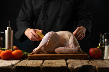 The carcass of a turkey, chicken lies on a cutting wooden board. The chef rubs the carcass with half a cut fresh lemon. Ingredients. Wooden texture. Black background. Culinary blog, cookbook.