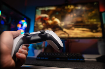 A gamer with a joystick in his hand plays an interesting video game with friends online on a large TV screen. Hobbies, gaming, fun activities, prizes, win. Neon lighting. © Anton
