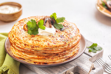 Savory thick crepes made of mashed potato, with fried mushrooms and sour cream. Light background. Close-up.