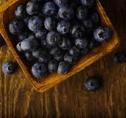 macro photography. Lots of fresh blueberries in a square bowl and on the table. Wooden texture. High angle view. Cooking, vitamins, antioxidants, healthy eating. Restaurant, hotel. advertising.