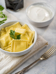 Beautifully set table for one person. Ravioli in a bowl with a sprig of parsley on top, fork, sour cream sauce. White background. Close-up. There are no people in the photo. Advertising, culinary blog
