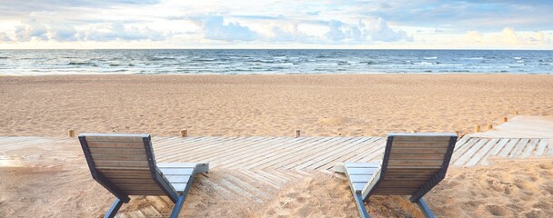 An empty modern wooden promenade through the sandy shore of the Baltic sea, sun lounger close-up. Sport, recreation, cycling, nordic walking, relaxation, vacations, weekend, tourism, leisure activity