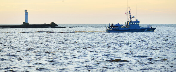 US coast guard ship sailing near the lighthouse at sunset. International (global) security theme
