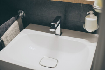 Closeup view of a sink with towels, toothbrush and soap dispenser. Modern environment bathroom fixtures with steel faucet. Cleanliness, health, recycling, pollution, cleaning, ethics, hygiene concept