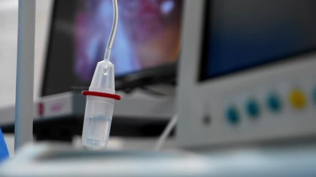 Close up isolated dropper of intravenous drug infusion system against the backdrop of a against the background of the display surgical monitor. IV drip during surgery to remove a cancerous tumor.