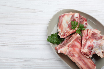 Plate with raw chopped meaty bones and parsley on white wooden table, top view. Space for text