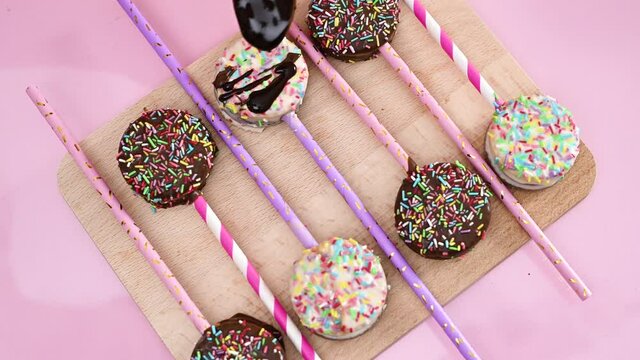 Decorating delicious sweet cake pops on wooden board with melted black chocolate 