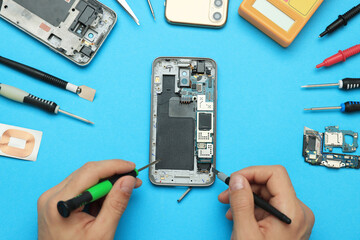 Man repairing broken smartphone on light blue background, top view