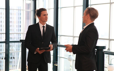 two young business people working and communicating while standing at the office with city building background.