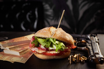 closeup of sandwich with ham cheese salad tomato garnished by gun and money on table