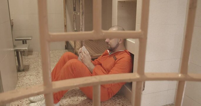 joyful prisoner in orange uniform opens a letter while sitting on the floor