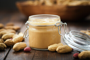 Bowl of peanut paste and fresh nuts. Jar of raw organic peanut butter on background.
