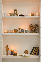 Burning wax candles and different decor on shelves