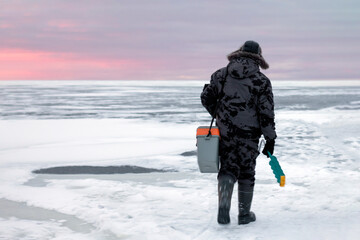 Fototapeta na wymiar A fisherman walks on the ice with a drill. Winter fishing.