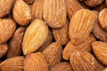 Close-up photo of almonds. Almond in foreground right in selective focus. There are salt crystals on the roasted almonds.