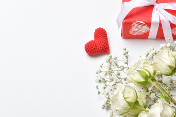 A holiday card with white roses, a red gift and a red knitted heart. Banner for Valentine's Day. Background on February 14.