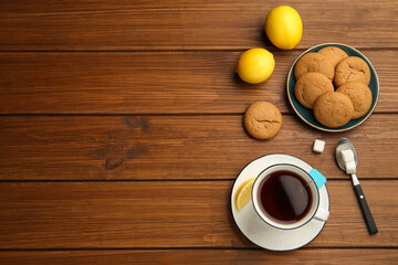 Flat lay composition with tea bag in ceramic cup of hot water, cookies and lemon on wooden table. Space for text