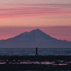 Adventure girl hiking in Alaska with Volcano Mountain in background during purple red and orange...