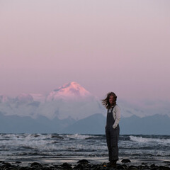 Adventure girl hiking in Alaska with Volcano Mountain in background during purple red and orange...