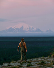 Adventure girl hiking in Alaska with Volcano Mountain in background during purple red and orange...