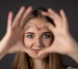 Fototapeta premium Young woman smiling and showing heart shape gesture with her fingers.