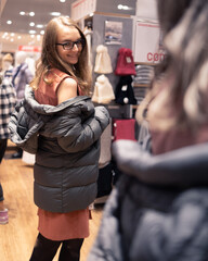Young woman trying on a coat in store in front of mirror.