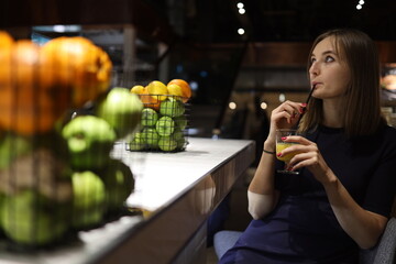 Young woman sitting in bar and drinking orange juice or cocktail.