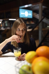Young woman sitting in bar and drinking orange juice or cocktail.