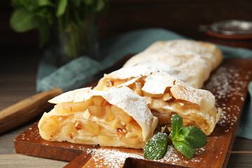 Delicious apple strudel with almonds, powdered sugar and mint on wooden board, closeup