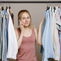 Pretty white woman shrugs her shoulders, doubting what to wear, Insecure woman standing near a clothes rack, not knowing what to wear to work. Nothing to wear and the concept of clothes