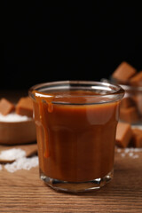 Tasty salted caramel in glass on wooden table