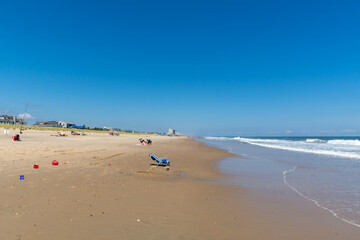 Fototapeta na wymiar REHOBOTH, DELAWARE - USA - AUGUST 17, 2020: A relatively empty beach south of Rehoboth Beach on a sunny summer afternoon. Empty beach chair in foreground and town of Rehoboth in background.
