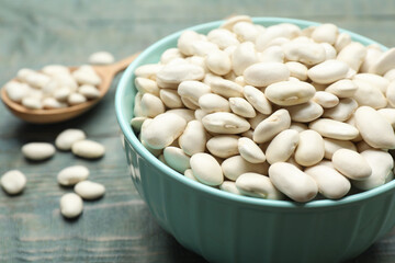 Bowl of uncooked white beans on blue wooden table, closeup
