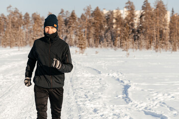 Fototapeta na wymiar Full length of a happy middle-aged athlete running in nature on a snowy winter day. Outdoor fitness, cardio training, outdoor exercises