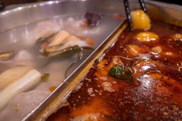 Close up of chopstick and boiling hotpot with 2 kind of soup.