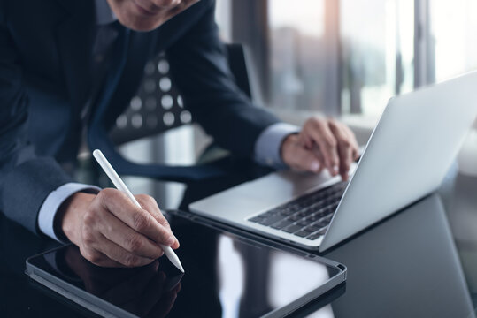 Asian businessman using stylus pen signing e-document on digital tablet with laptop computer on table at office, e-signing, electronic signature, paperless office