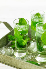 Summer Sweet Refreshing Mint Liqueur Cocktail Shots with Ice and Mint Leaves on White Wooden Background. Selective focus.