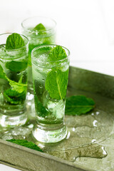 Fototapeta na wymiar Summer Sweet Refreshing Mint Liqueur Cocktail Shots with Ice and Mint Leaves on White Wooden Background. Selective focus.