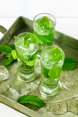 Summer Sweet Refreshing Mint Liqueur Cocktail Shots with Ice and Mint Leaves on White Wooden Background. Selective focus.