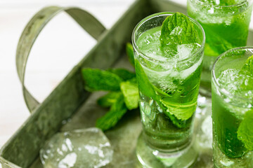 Summer Sweet Refreshing Mint Liqueur Cocktail Shots with Ice and Mint Leaves on White Wooden Background. Selective focus.