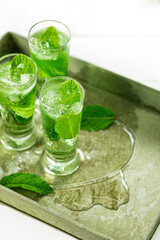 Summer Sweet Refreshing Mint Liqueur Cocktail Shots with Ice and Mint Leaves on White Wooden Background. Selective focus.