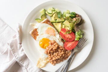 High angle closeup of homemade vegetarian brunch plate, including eggs, avocado, beans, tomato, salad, lettuce, with cutlery and napkin