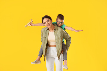Teenage girl carrying pickaback her little brother with wooden airplane on yellow background