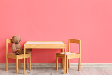 Wooden table and chairs with cute bear toy near color wall
