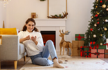 Beautiful young woman with cup of hot chocolate at home on Christmas eve