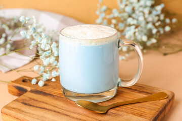 Wooden board with cup of blue matcha latte and gypsophila flowers on color background