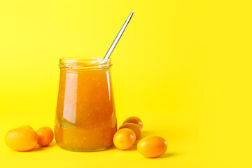 Jar of tasty kumquat jam and fresh fruits on yellow background